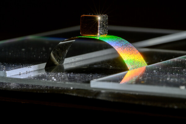 A metallic arch on a surface reflecting a rainbow prism.