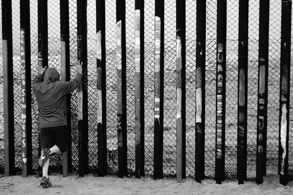 Young person pressing hands up against a border wall.