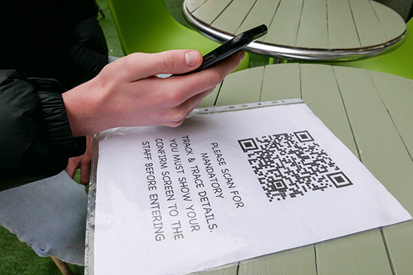 Person scanning QR code on their phone from a sign that reads PLEASE SCAN FOR MANDATORY TRACK AND TRACE DETAILS. YOU MUST SHOW YOUR CONFIRM SCREEN TO THE STAFF BEFORE ENTERING.