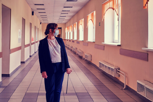 Teacher wearing face mask standing alone in a school hallway.
