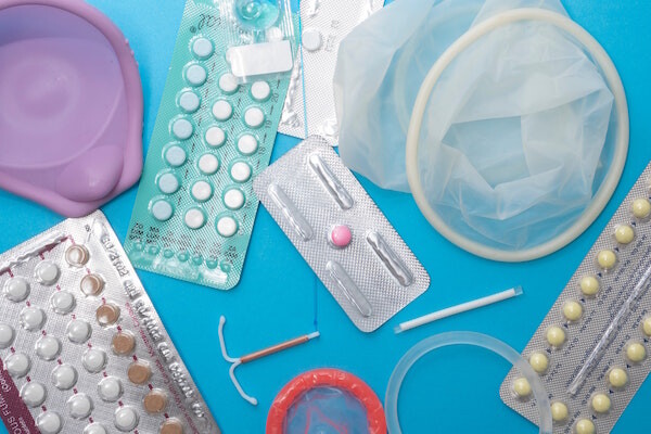 A flat lay of bIrth control pills, IUDs, condoms, and other contraceptives against a blue background