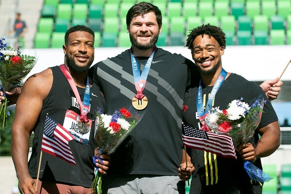 From left, Reggie Jagers, Mason Finley, and Sam Mattis make up to the U.S. men’s discus team. They are holding flowers an American flags and have their medals around their necks.