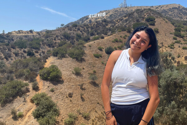 Student standing outside on hill with Hollywood sign behind her