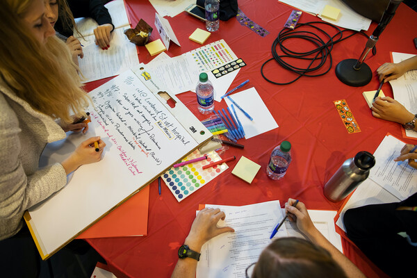 Students work at a table covered with paper, water bottles and markers.
