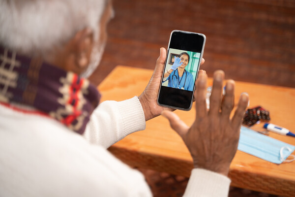 Elderly African American person waves to a doctor via telemedicine on their smartphone.