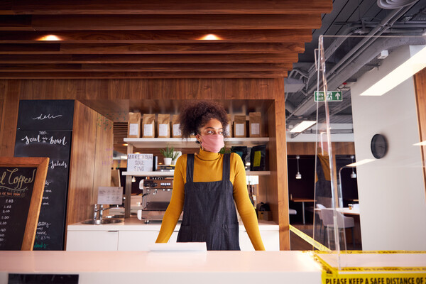 Coffee shop employee wearing a face mask stands behind a counter.