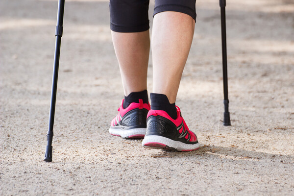Closeup of person’s calves, wearing running shoes accompanied with walking sticks.