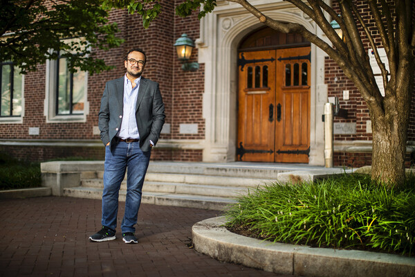 Hasan Küçük stands with his hands in his jeans pockets in front of the wooden double doors and red brick facade of  Fisher-Bennett Hall