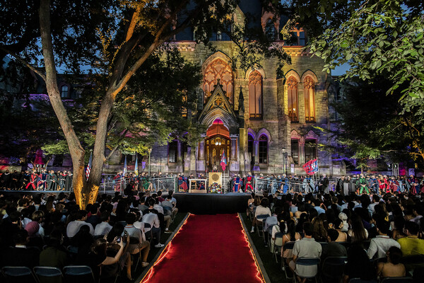 Front of College Hall lit up with red and blue lights during Convocation with students seated on lawn.