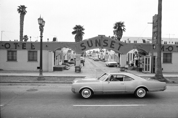 a 1960s car parked in front of the motel sunset in los angeles