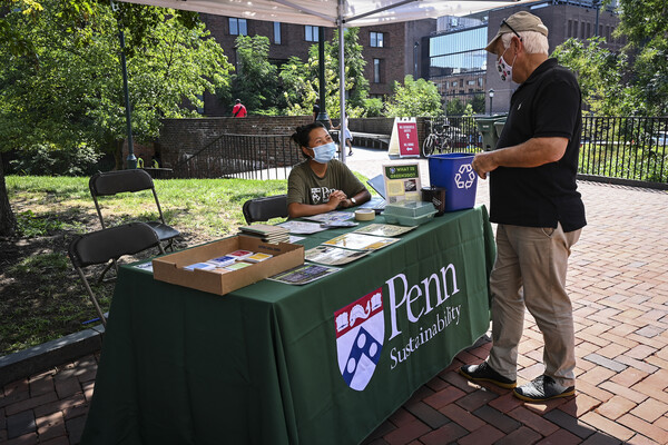 A person seated at a table labeled Penn Sustainability interacts with someone visiting the table