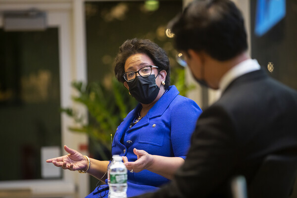 Former attorney general of the United States Loretta Lynch, wearing glasses, a black surgical mask and a blue suit dress, gestures as the speaks to a man in the foreground