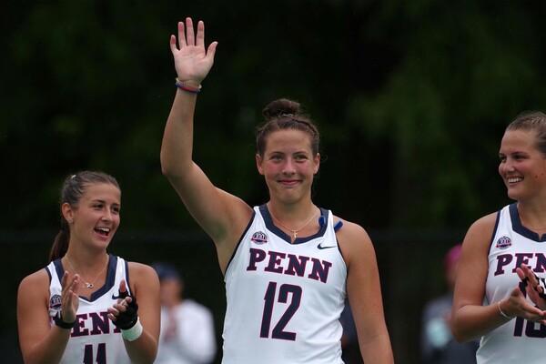 Wearing her white Penn jersey, Gracyn Banks waves to the crowd while standing between two teammates.