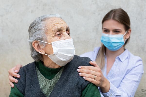 Young person with hands on the shoulders of an older person, both wearing face masks.