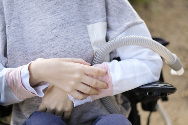 Hands of person with muscular dystrophy holding a breathing apparatus.