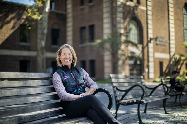 On a wooden bench outside of the Palestra, Andrea Wieland sits while wearing a blue vest with the works Penn on it.