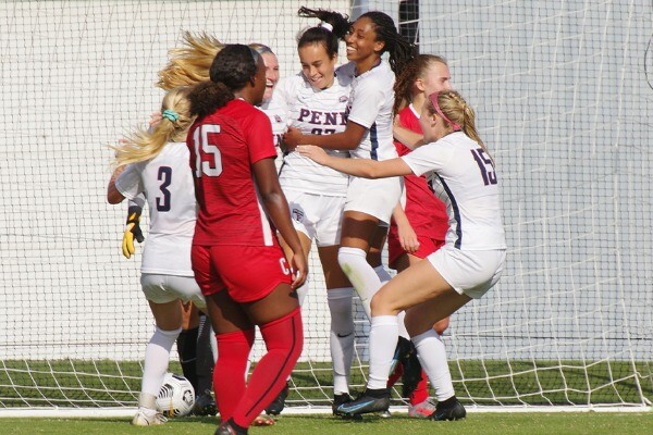 At Rhodes Field, players on the women's soccer team hug and celebrate near the net after scoring a goal.