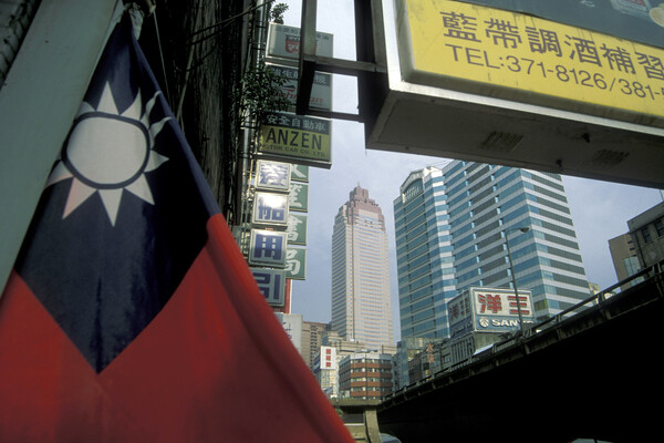 a taiwanese flag is in the foreground with skyscrapers and shop signs in Chinese and English in the background