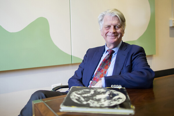 Design School Dean Fritz Steiner seated behind table in front of abstract green and white painting