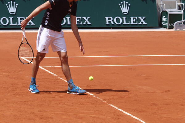 Tennis player preparing to serve on a clay court with Rolex signs on wall of court in background.