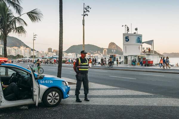 Police officer stands in front of his car on a street near the ocean boardwalk in Rio de Janeiro, Brazil