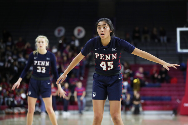 At the Palestra, Kayla Padilla, wearing her blue Penn jersey, plays defense with her arms stretched out to the side. A teammate stands behind her.