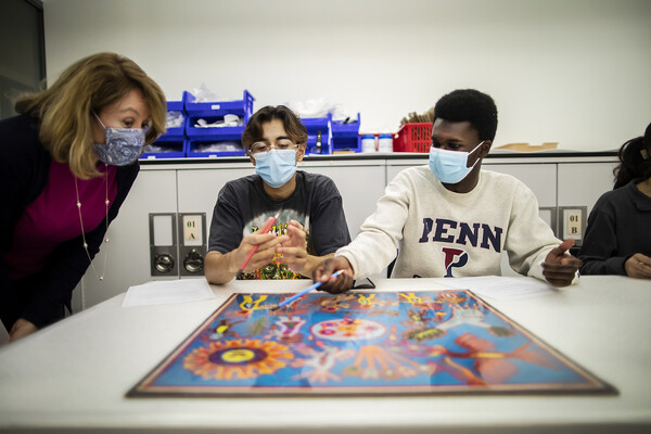 professor and two students looking at colorful artwork on table 