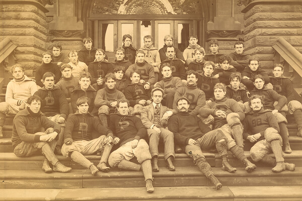 Members of the 1895 football team sit on the steps wearing Penn sweaters.