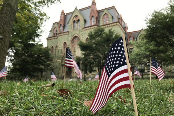 Many small flags placed in the grass on College Green in front of College Hall.