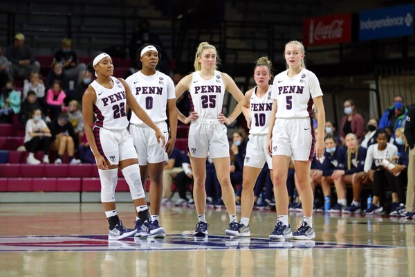 Wearing their white Penn jerseys, five members of the women's basketball team stand at center court.