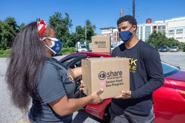 Onika Washington-Johnson hands a box of food to David Cabello in a parking lot.