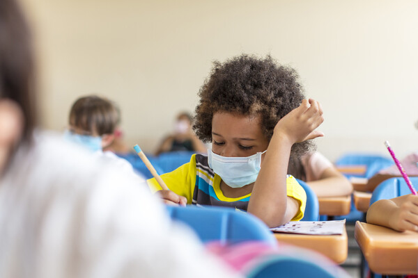 Child wearing mask in school writes at a desk