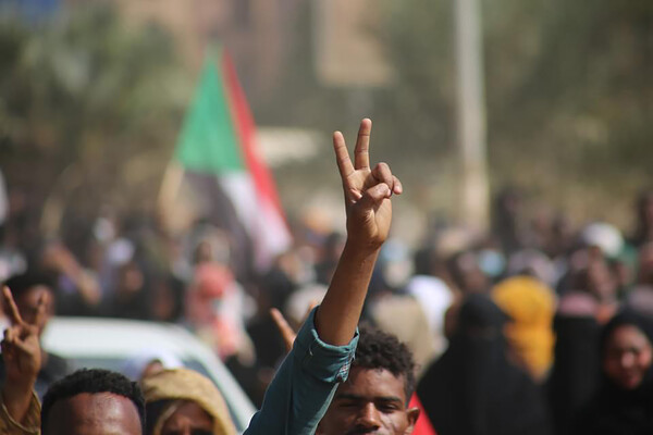 Person in streets of Sudan in a protest crowd flashes the peace sign.