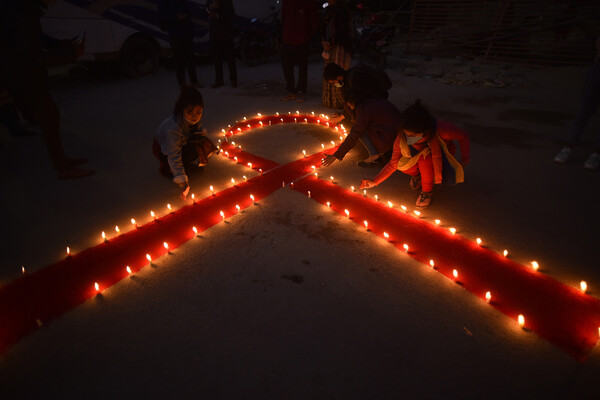 People light red candles in the shape of an AIDS awareness ribbon as darkness sets in