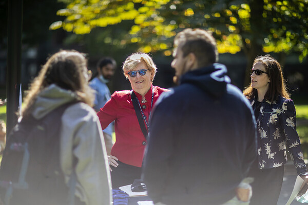 Maureen Rush, wearing red, with hands on hips talks and smiles with people on campus