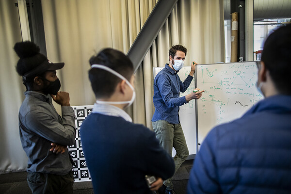 one person writing out math equations at a white board while talking to three other people all of whom are wearing masks