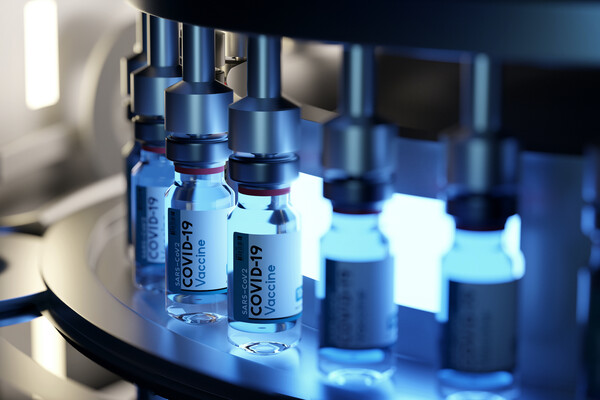 Vials labeled "SARS-CoV-2 COVID-19 Vaccine" lit up with neon light on a machine filling them.