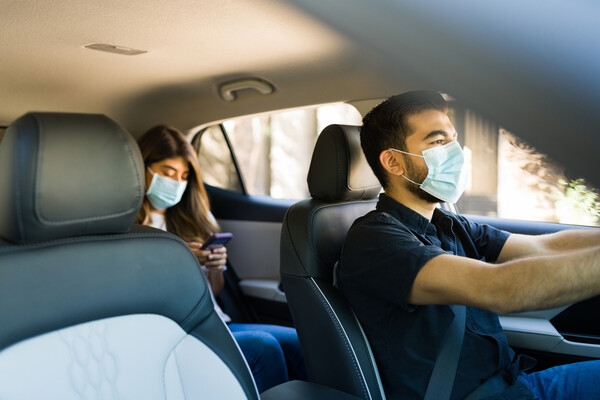 Rideshare driver driving a passenger, both are wearing face masks.