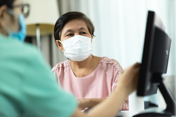 Patient with a face mask looking at a computer with a medical professional.
