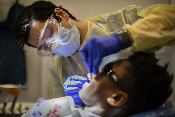 Dental hygienist wearing a mask and goggles cleans the teeth of a patient.