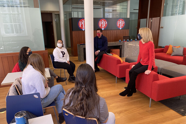 Penn president Amy Gutmann sits in a lounge with four students.