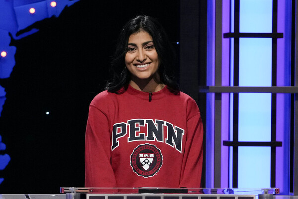 a smiling student wearing a Penn sweatshirt stands in front of a game show platform