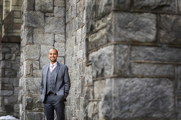 A man in a three-piece suit stands in front of a stone building