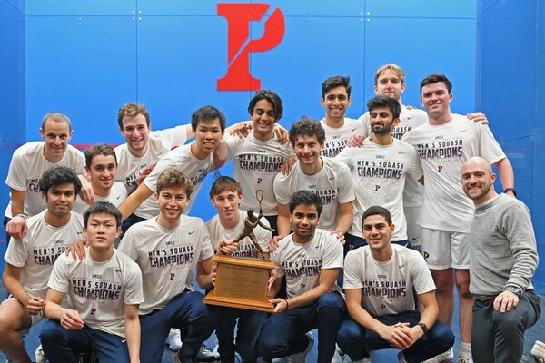 Wearing men's squash champions t-shirts, members of the men's squash team pose with the championship trophy.