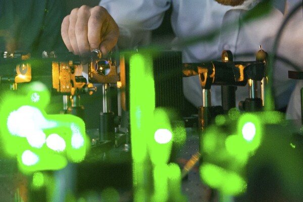 a close up of hands adjusting a lens on an optics table with green laser light in the foreground