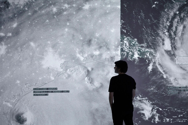 Person standing in front of two giant panels of film projected on the wall of NASA footage of a storm on planet Earth. 