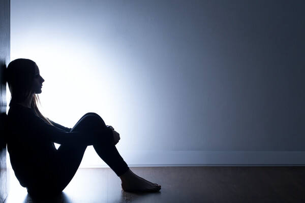 Silhouette of a person sitting against a wall on the side of the image, legs pulled up close to her chest.