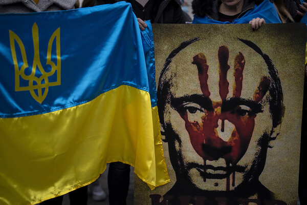 A Ukrainian flag is shown in front of a spray painted image of Vladimir Putin with a red handprint on his face