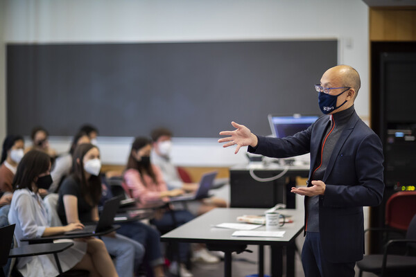 A man in a blue suit gestures as he teaches a class
