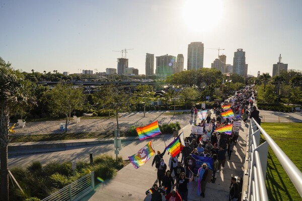 Marchers waving gay pride flags make their way long a boardwalk with the skyline of St. Petersburg, Florida, in the background